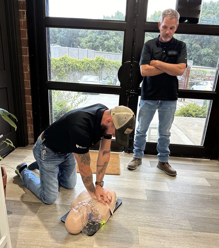 A student kneeling to practise chest compressions on a CPR manikin while the instructor observes