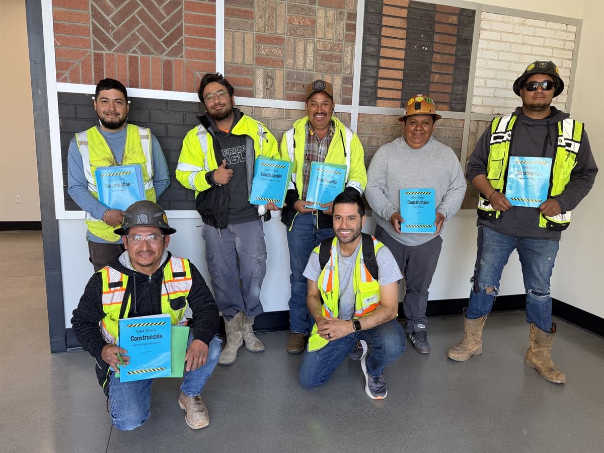 A crew holding their Spanish-language course books with Edwin Cueva after OSHA 30 training